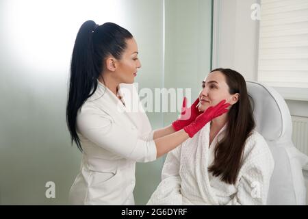 Cosmétologue regardant la femme visage vérifier l'état de la peau pendant l'examen de la peau dans le salon de beauté Banque D'Images