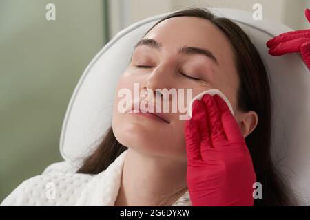 Un cosmétologue nettoie le visage d'un patient avec un tampon de coton dans un salon de beauté et de spa se préparant à l'intervention Banque D'Images