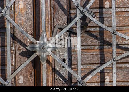 La vieille porte avec une poignée en fer forgé derrière une treillis de fer avec décoration, gros plan. Banque D'Images