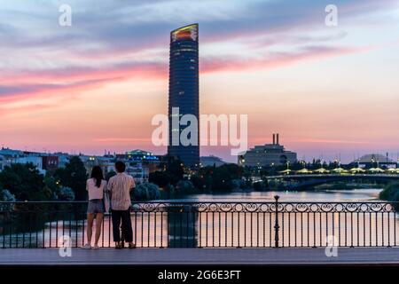 Couple debout sur le pont au coucher du soleil, Puente de Triana, vue sur le fleuve Rio Guadalquivir, dans le gratte-ciel arrière Torre Sevilla, Séville Banque D'Images