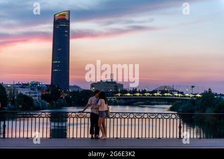 Couple debout sur le pont au coucher du soleil et embrassant, Puente de Triana, vue sur le fleuve Rio Guadalquivir, dans le gratte-ciel arrière Torre Sevilla Banque D'Images