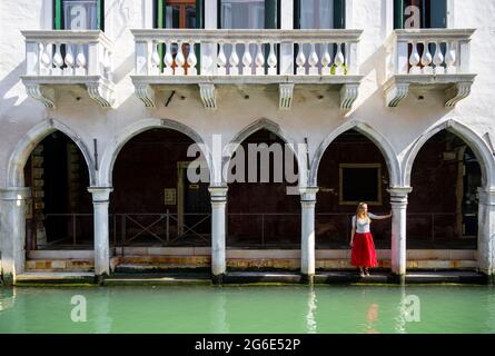 Jeune femme debout dans un portique près d'un canal, Venise, Vénétie, Italie Banque D'Images