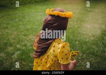 vue arrière gros plan des longs cheveux d'une fille qui coule dans le vent avec une couronne de pissenlits sur sa tête avec une pelouse bien taillée sur le fond Banque D'Images