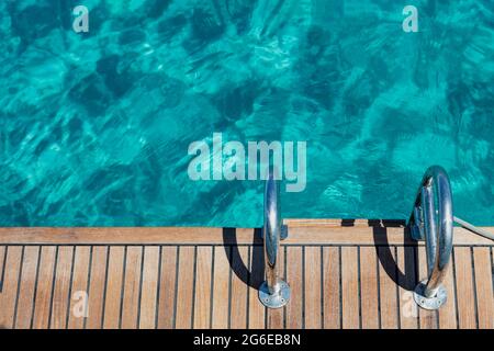 Bateau à voile terrasse, bois de teck et échelles métalliques, fond bleu turquoise de l'eau de mer. Yacht amarré, pour nager dans la mer Egée, Grèce. Espace, su Banque D'Images