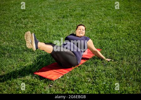 Exercice de levage de jambe effectué par le corps positif femme obèse sur la pelouse. Banque D'Images