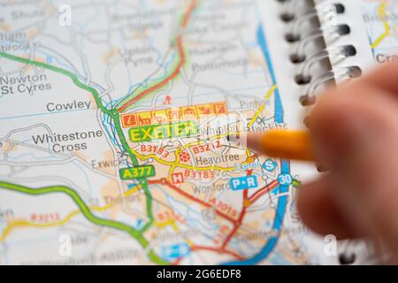 Gros plan d'une page sur une carte routière imprimée atlas avec la main d'un homme tenant un crayon pointant vers la ville d'Exeter en Angleterre. Concept : lecture de cartes Banque D'Images