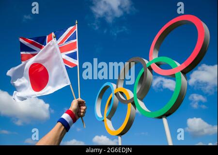 RIO DE JANEIRO - MARS 2016 : l'athlète tient des drapeaux japonais et britannique ensemble devant un grand ensemble d'anneaux olympiques sous un ciel bleu vif. Banque D'Images