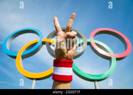 RIO DE JANEIRO - MARS, 2016: Une main portant le Japon couleurs rouge et blanc bracelet fait une victoire, V-signe geste devant les anneaux olympiques. Banque D'Images