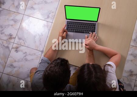 Photo aérienne d'un couple utilisant l'ordinateur portable ensemble, ils regardent l'écran. Maquette d'un PC portable. Ordinateur à écran vert. Banque D'Images