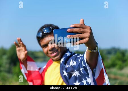 Main avec un smartphone de jeune homme couvert d'un drapeau américain prenant le selfie Banque D'Images