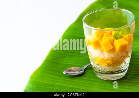 Le riz collant de mangue et le lait de noix de coco dans le verre a mis sur la feuille de banane. Concept de dessert d'été. Banque D'Images