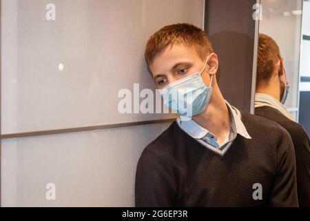 Un type de nationalité caucasienne est assis dans un coin portant un masque protecteur triste au miroir. Banque D'Images