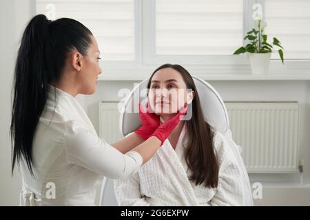 Cosmétologue vérifiant l'état de la peau du visage pendant l'examen de la peau dans le salon de beauté. Concept professionnel de contrôle de la peau Banque D'Images