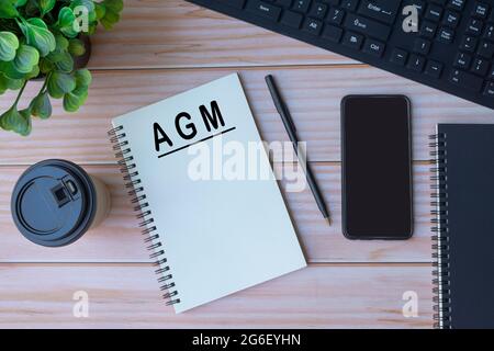 Texte AGM sur bloc-notes avec clavier, stylo, café et smartphone sur table en bois Banque D'Images