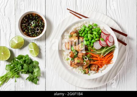 bol à poke de tofu avec riz basmati, haricots édamames, radis, concombre finement coupé et carottes dans un bol blanc avec baguettes, vue horizontale de l'abov Banque D'Images