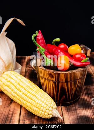 Épis de maïs avec piments et tomates légumes frais nourriture naturelle dans seau en bois, bio Banque D'Images