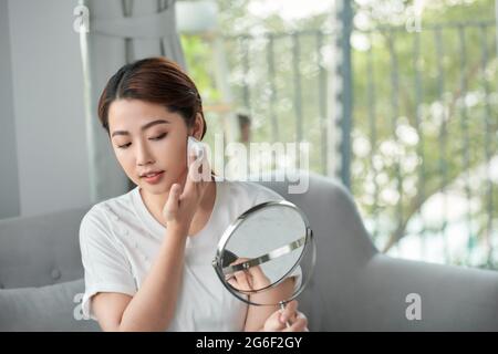 Joyeuse jolie femme asiatique appliquant de la poudre transparente sur sa peau fraîche et claire Banque D'Images