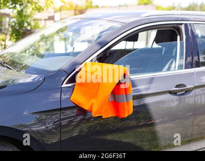 Un gilet d'avertissement orange est suspendu sur le rétroviseur d'une voiture de tourisme. Concept de panne de voiture, signal d'assistance routière, problèmes Banque D'Images