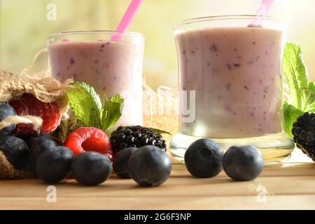 Smoothie de yogourt aux baies forestières en verre sur table en bois avec sac plein de myrtilles, framboises de mûre avec fond vert de forêt de clo Banque D'Images