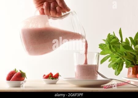 Servir le milkshake de fraise d'une carafe dans un verre sur une table en bois avec des bols avec des fruits. Vue avant. Banque D'Images