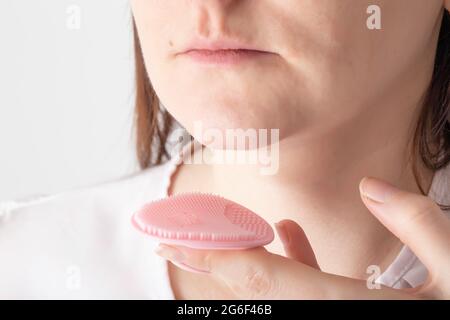 La fille tient une brosse en silicone pour nettoyer le visage avec une mousse de gel pour nettoyer les pores de la peau sur le menton Banque D'Images