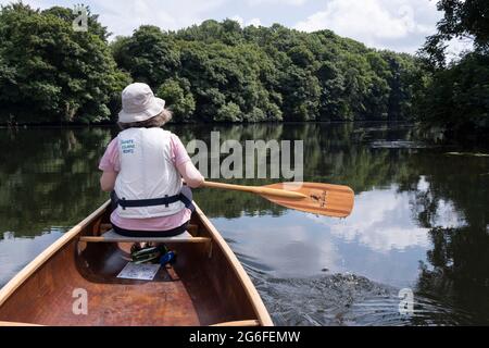 La vue arrière d'une femme canoéiste qui pagayer sur la rivière Yare près de Thorpe St Andrew, le 2 juillet 2021, à Norwich, Norfolk, Angleterre. Banque D'Images