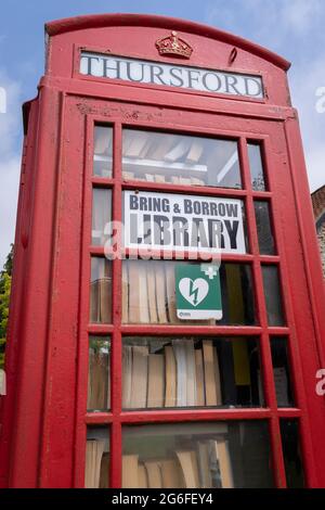 L'ancien kiosque téléphonique qui dessert maintenant la communauté du village local avec un service de bibliothèque de livres d'emprunt et de prêt, sur un viillage vert dans la campagne de Norfolk, le 27 juin 2021, à Thurford, Norfolk, Angleterre. Banque D'Images