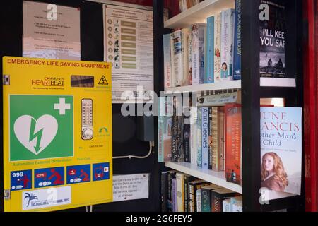 Un intérieur d'un ancien kiosque téléphonique qui dessert maintenant la communauté du village local avec une bibliothèque de livres à emporter et à emprunter et de l'équipement de défribrilleur salvateur, sur un viillage vert dans la campagne de Norfolk, le 27 juin 2021, à Thurford, Norfolk, Angleterre. Banque D'Images