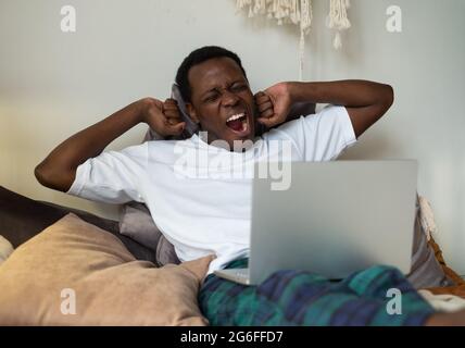 Homme africain travaillant allongé sur le lit à la maison étant fatigué bâilling. Banque D'Images