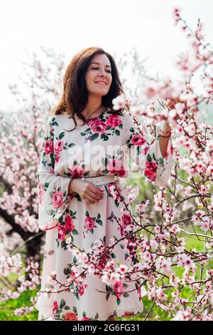 Belle femme brune dans une robe avec des fleurs marche à travers le jardin fleuri au printemps Banque D'Images