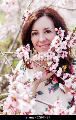 Belle femme brune dans une robe avec des fleurs marche à travers le jardin fleuri au printemps Banque D'Images