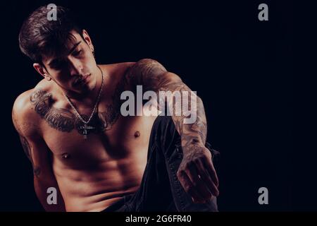 Jeune homme avec tatouages assis avec une expression pensive. Banque D'Images