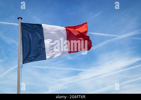 Le drapeau français sur le mât flotte dans le vent contre le ciel bleu. Banque D'Images