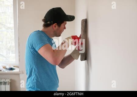 Ouvrier de main avec couteau à mastiquer travaillant sur le remplissage de mur d'appartement Banque D'Images
