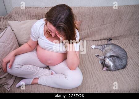 La femme enceinte se tient à une tête douloureuse à l'intérieur de la maison, le mode de vie Banque D'Images