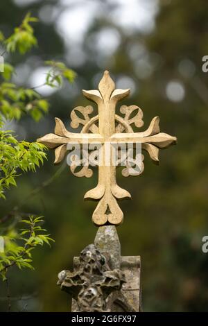 Croix plaquée or sur le dessus de la pierre tombale dans le cimetière de la cour de l'église. Orné et entouré d'arbres verts la journée d'été. Enterrement chrétien en forme de croix Banque D'Images