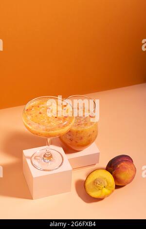 Jus de fruit boisson à base de pêche mûre fraîche dans un verre sur un podium orange moderne et abstrait Banque D'Images