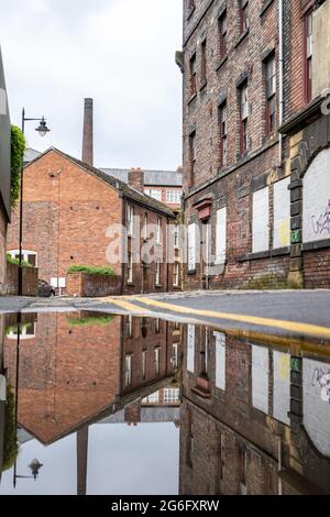Vieille rue industrielle avec une allée pavée, des chalets et de vieux bâtiments d'usine reflétés comme une image miroir dans les eaux d'inondation sur la route. Personne. Banque D'Images
