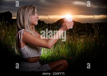 Fille blonde pratiquant la méditation au coucher du soleil avec une bougie Banque D'Images