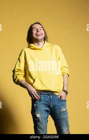 Un homme heureux en Jean et un sweat à capuche riant sur fond jaune Banque D'Images