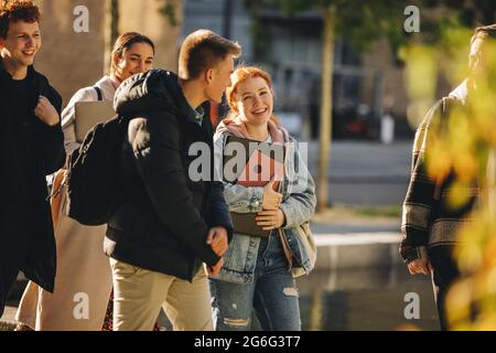 Fille souriante marchant avec des amis à l'extérieur à l'école secondaire. Des étudiants joyeux qui marchent ensemble après le cours sur le campus universitaire Banque D'Images