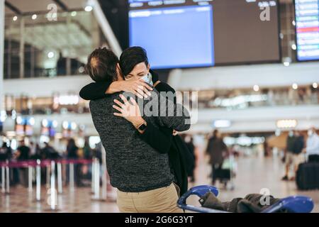 Une femme excitée rencontre son mari pendant une pandémie à la porte d'arrivée de l'aéroport. Homme donnant un câlin chaud à sa femme à son arrivée à l'aéroport en cas de pandémie. Banque D'Images