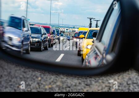 Embouteillage sur l'autoroute européenne avec une grande ville en arrière-plan - beaucoup de voitures dans la file d'attente vu depuis le rétroviseur intérieur Banque D'Images