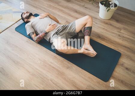 Jeune homme méditant et respirant profondément sur le tapis de yoga. Homme faisant un exercice de respiration diaphragmatique Banque D'Images