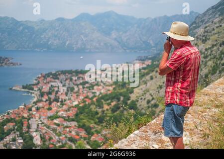 Homme en t-shirt et casquette tient le beau paysage de la nature et fait des photos sur appareil photo Kotor, Monténégro. Style de vie concept été vacances en plein air. Banque D'Images