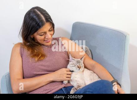 jeune latina petant son chat endormi dans une chaise Banque D'Images