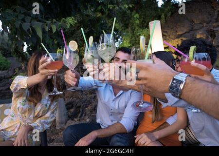 Groupe de jeunes qui se réunissent sur la terrasse du jardin pour un cocktail en levant leurs verres pour un toast festif. Banque D'Images