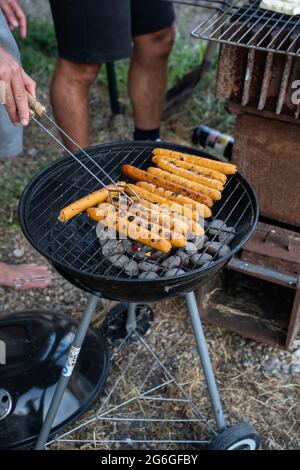 Avoir un barbecue avec des coals chauds à l'extérieur, la culture de saucisses avec des pinces sur un barbecue ou un barbecue, vertical. Banque D'Images