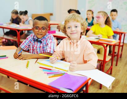 Deux petits enfants d'élèves du primaire préparent une leçon assis à un bureau avec des crayons de couleur dans leurs mains Banque D'Images