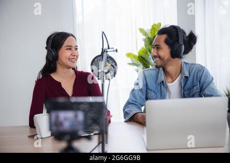 Deux radios asiatiques hébergent un podcast dans un studio de diffusion, une femme asiatique parlant au micro avec un homme en ligne à la maison Banque D'Images